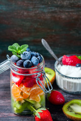 Healthy homemade fruit salad in a jar on rustic wooden background.