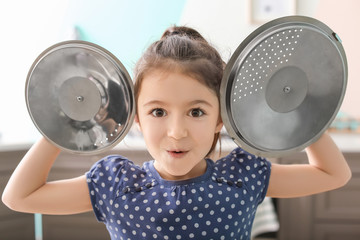Cute little girl playing with saucepan caps as cymbals in kitchen