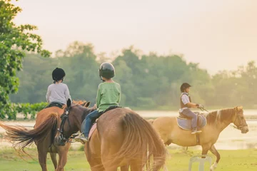 Poster Kinderen leren voor zonsondergang paard te rijden in de buurt van de rivier. © JinnaritT