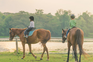 Kids learn to ride a horse near the river before sunset.