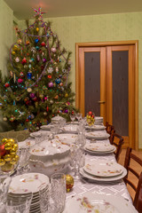 Served table with festive tableware near beautiful decorated Christmas tree in living room interior. Concept of new year holiday at cozy home