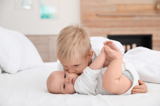 Cute boy kissing his little sister on bed at home