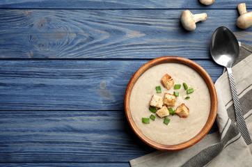 Flat lay composition with bowl of fresh homemade mushroom soup and space for text on wooden background