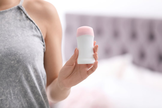 Beautiful young woman holding deodorant in bedroom, closeup. Space for text