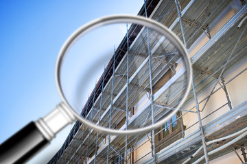 Metal scaffolding with plastic grid for the restoration and reconstruction of the plaster facade of an old building - concept image seen through a magnifying glass