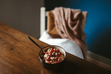 Eine Schüssel Porridge und Weintrauben auf einem Holztisch mit Stuhl und Decke im Hintergrund