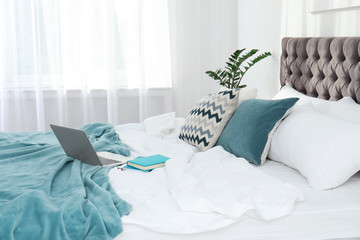 Laptop and books on bed in stylish room interior