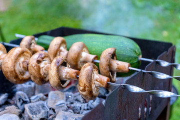 Mushrooms and zucchini on skewers are fried on coals