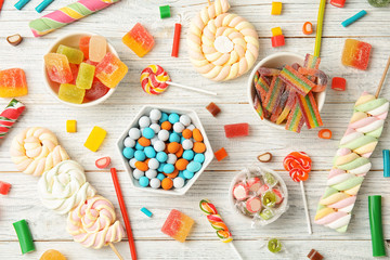 Many different yummy candies on white wooden background, top view