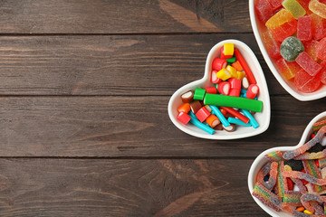 Flat lay composition with different yummy candies in heart shaped bowls and space for text on wooden background