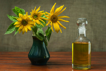 Sunflower oil in a glass decanter and a sunflowers in a vase on a background of burlap.