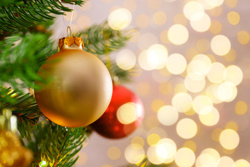Decorated Christmas tree on soft yellow lights with bokeh effect background. Festive composition with fir and blurry sparkling backdrop, new year holiday decorations. Close up, copy space.