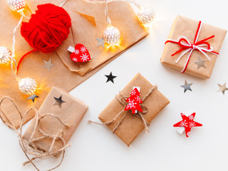 DIY presents wrapped in craft paper. Gifts tied with white and red threads with red heartm star, fir tree symbols. Metal light bulbs with delicate pattern.