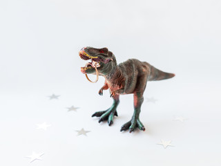 Dinosaur with engagement ring. Plastic toy with wedding jewelry. White background with star confetti.