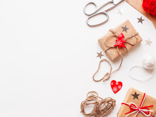 DIY presents wrapped in craft paper. Gifts tied with white and red threads with red heart symbol. Christmas and New Year holiday background.