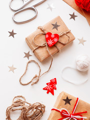 DIY presents wrapped in craft paper. Gifts tied with white and red threads with red heart symbol. Christmas and New Year holiday background.