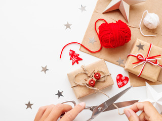 Woman wrapping DIY presents in craft paper. Christmas and New Year gifts tied with white and red threads with toy train as decoration.