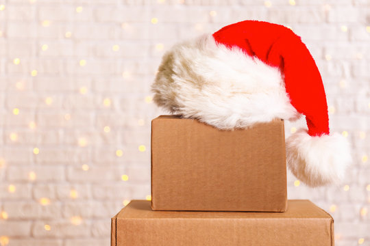 Blank brown freight box with Santa Claus hat on top, brick wall with Christmas lights on background. Moving company / delivery service holiday deals promotion concept. Copy space, close up.