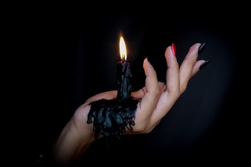 Black Candle melted on hand in black background. For halloween's concept. Felling darkness with light of flame burning from the supernatural. - Powered by Adobe