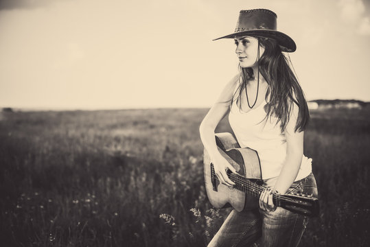 young countryside girl playing guitar at rural field background