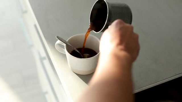 Man pouring hot aromatic coffee into cup at table, closeup. Lazy morning
