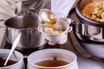 Meat pelmeni, are served with meat broth in a flat dish 