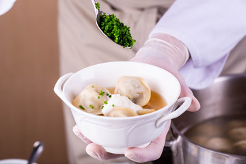Boiled meat pelmeni, are served with meat broth, sour cream and fresh greens