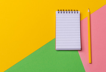 Blank notebook and a pencil on a colorful desk. Above view. Minimalist style.