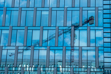 Fototapeta na wymiar Construction crane reflected in modern glass facade, construction industry concept.