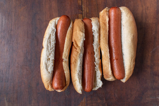 row of plain hot dogs in buns flat lay on wood table