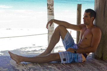 Junger Mann sitzt an Palme angelehnt am Strand von Xpu Ha in Mexico auf der Halbinsel Yucatan bei...