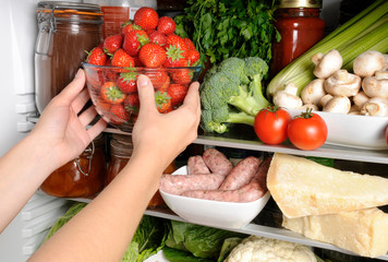WOMAN TAKING BOWL OF FRESH STRAWBERRIES FROM REFRIGERATOR