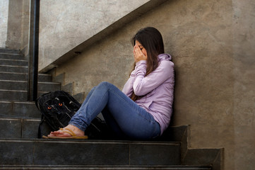 depressed student woman or bullied teenager girl sitting outdoors on street staircase scared and...