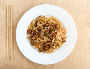 Noodles wok on a white plate. Rice noodles cooked in wok on a white plate. The dish is on a wooden surface.