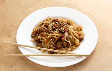 Noodles wok on a white plate. Rice noodles cooked in wok on a white plate. The dish is on a wooden surface.