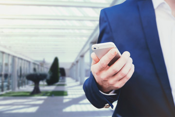Businessman in a blue jacket and white shirt holding a smartphone in his hand on the background in the business center