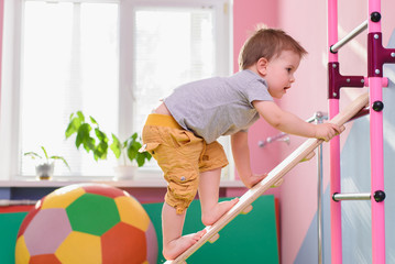 the little boy climbs up a wooden plate in the gym