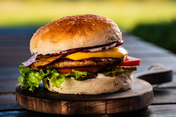 Juicy tasty cheeseburger with beef, lettuce, pickles, tomato and onion rings on a wooden table. Classic street food - grilled burger