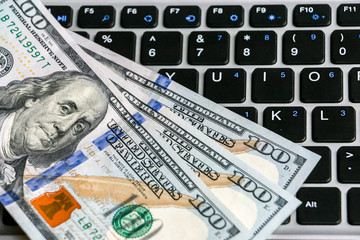 Closeup view of one hundred dollar banknotes lying on the laptop keyboard.