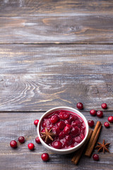 Homemade spicy cranberry sauce with fresh cranberries, cinnamon and star anise on a wooden background, free space © olepeshkina