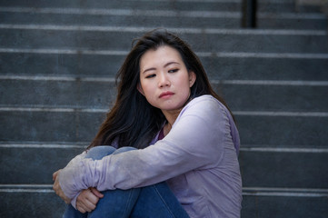 depressed Asian Japanese student woman or bullied teenager sitting outdoors on street staircase...