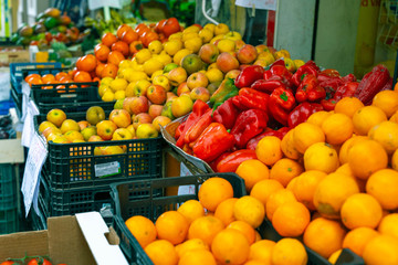 Street  fruit and vegetables market. Oranges, peppers, apples, kakis, tomatoes.Shallow depth of field, focus on peppers.