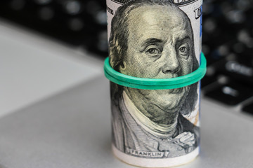 Closeup view of one hundred dollar banknotes lying on the laptop keyboard.