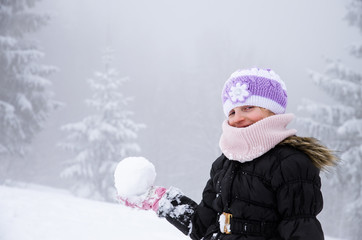 child with snowball in winter forest