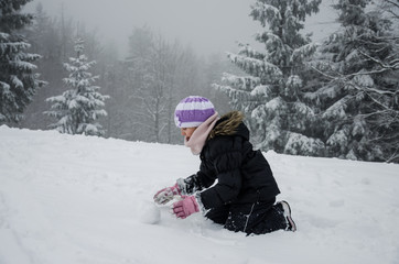 child with snowball in winter forest