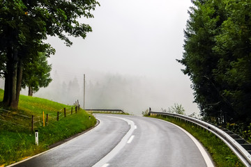 Beautiful mountain road in Austria. Misty forest and cloudy sky in background.