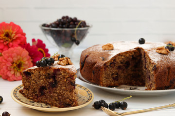 Homemade pie with black currant and walnuts is located on a plate on a white background.  In the foreground is a piece of cake