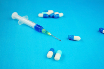 A detailed macro of a syringe by pills with needle and blue background