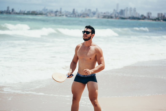 Young Brazilian man playing beach tennis on the beach with swimwear