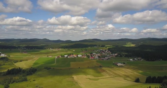 Aerial, descending, drone shot, away from a small town in the french countryside, cloud shadows reflecting on the ground, in Chapelle des bois, Doubs and Jura regional park, Franche comt&radic;&copy;, in France